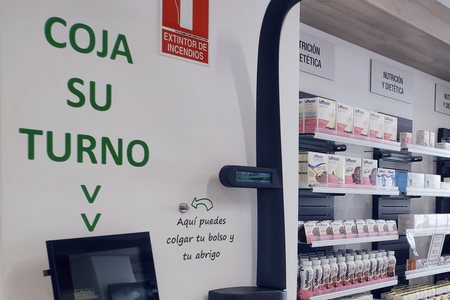 Zona de atención de una Farmacia Amiga: el expendedor de turnos, el aviso de «coja su turno» y los lineales de nutrición y dietética.